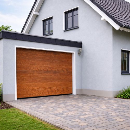 Porta garage sezionale effetto legno installata su casa moderna con facciata grigio chiaro, infissi antracite e pavimentazione esterna in autobloccanti.