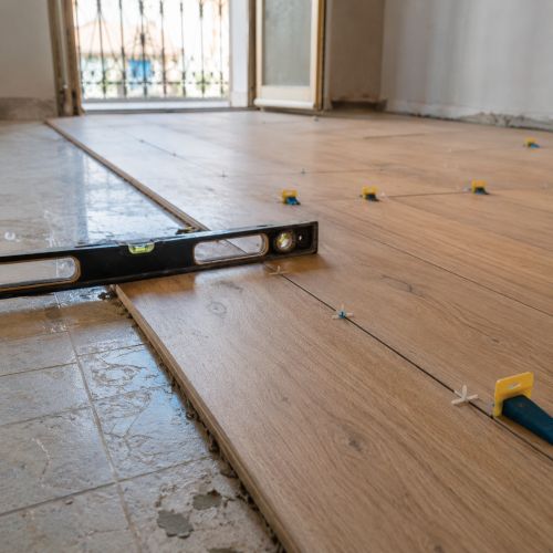 Posa di parquet sopra pavimento esistente con distanziatori e livella durante lavori di ristrutturazione interna.