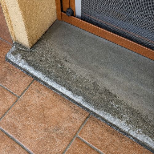 Dettaglio di una soglia in pietra serena davanti a una porta finestra in ambiente residenziale.