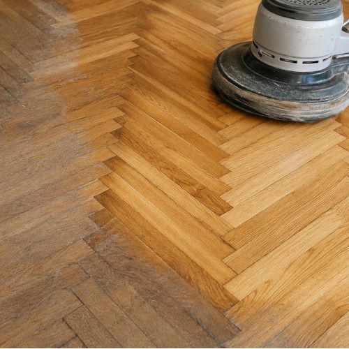 Parquet a spina di pesce sottoposto a un trattamento professionale, con una chiara differenza tra la zona ancora opaca e usurata e quella gi&agrave; levigata e lucidata. 
